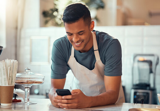 Phone, small business and barista man in cafe shop for networking, online sales management and ecommerce. Happy waiter, cashier or worker person on smartphone, technology application in restaurant