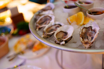 shells with oysters on a platter with ice, lemons and sauce. 