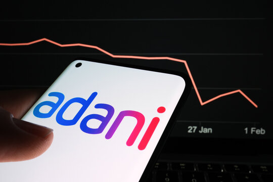 Adani Group logo seen on the smartphone screen and company stock price drop graph seen on the blurred background. Real stock chart for a recent month timeframe. Stafford, England, February 2, 2023