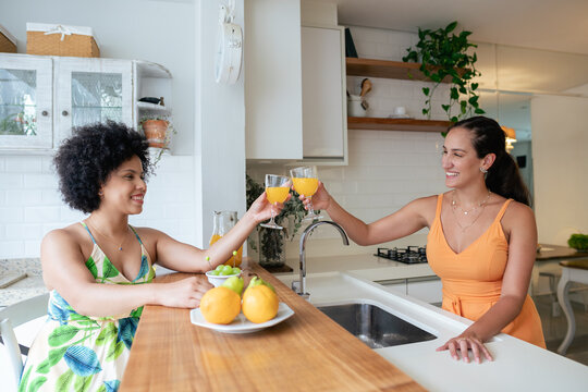 healthy friends celebrating with fresh orange juice in kitchen counter