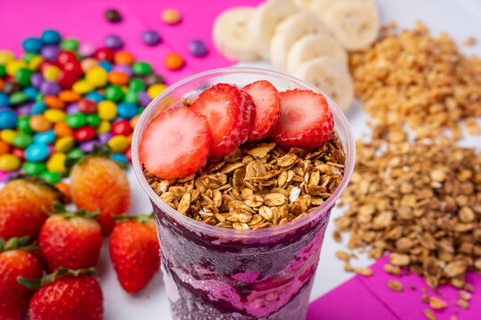 close up of acai or açaí cup with topping strawberry and granola in colorful background