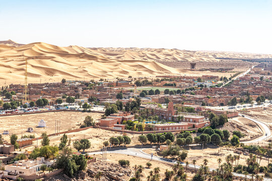 Elevated view from Baroun mountain in Taghit, Bechar. Sahara desert of Algeria with the Saoura hotel building and swimming pool, a mosque minaret and a soccer field. Trees, palm trees, and sand dunes.