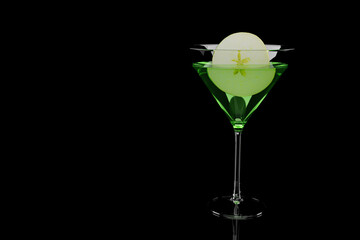 Green appletini cocktail with slice of apple in martini glass on black background
