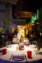 a table with a white tablecloth, glasses, crockery and decor in dark restaurant