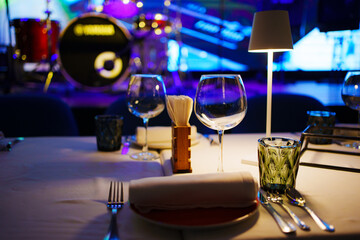 a table with a white tablecloth, glasses, crockery and decor in dark restaurant