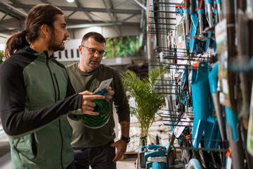 Obraz na płótnie Canvas A customer and a salesman are standing in front of a display of gardening tools. The salesman is explaining the tools to the customer.