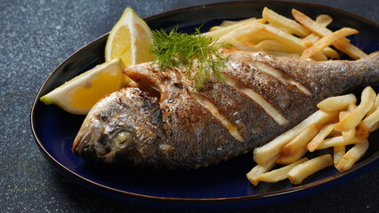 Grilled fish dorado in a plate with chips and lemon and herbs