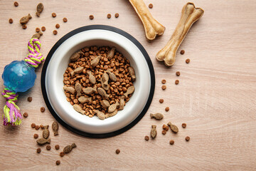 A bowl with dog food, dog treats and toys on a wooden floor.