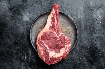 Raw cowboy steak, rib eye steak with bone, beef marbled meat on butcher cutting board. Black...