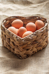 Free range chicken eggs in a heart shaped water hyacinth wicker basket. On a hessian sack cloth background