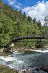 Fototapeta na wymiar Eine Fußgängerbrücke führt über den Fluss Passer im Passeiertal in den Südtiroler Alpen, Italien