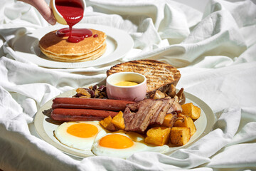 English breakfast: scrambled eggs with sausages, potatoes and bacon in a plate. Breakfast in bed - scrambled eggs and pancakes