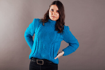 a woman in a blue sweater poses on a gray background
