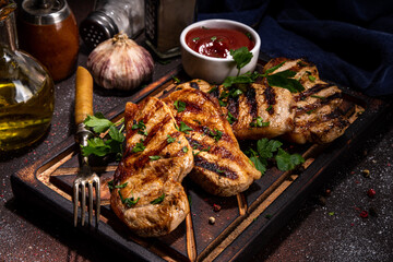 American bbq food concept. Grilled barbeque pork meat steaks with tomato bbq sauce, spices and greens, on cutting board, dark background top view copy space 