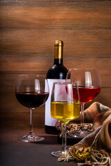 Winter autumn wine tasting, degustation set. Three glasses with various craft wine - pink, red and white, with bottle of wine on cozy wooden background with warm plaid, copy space