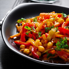 Vegetable stew of chickpeas, carrot, sweet peppers, onions, garlic and tomato sauce with lemon on the dark table. Oriental cuisine.