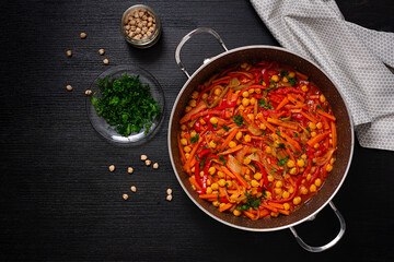Vegetable stew of chickpeas, carrot, sweet peppers, onions, garlic and tomato sauce with lemon on the dark table. Oriental cuisine. Top view