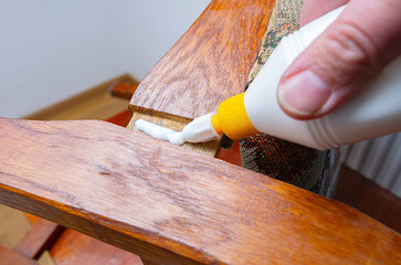 Applying white glue on broken wooden chair at home. Do-it-yourself home furniture repair, giving old things new life concept image. 