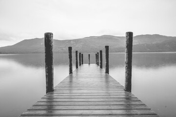 Naklejka na ściany i meble Derwentwater Jetty boat landing with wooden posts and long exposure to produce blurry out of focus water