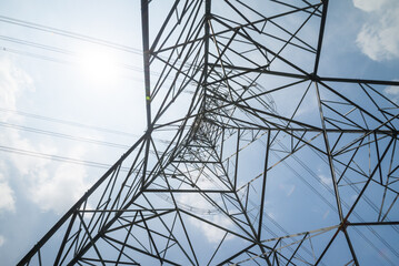 Structure pattern from bottom view of high voltage pole power transmission tower with clear sky sunshine day background. Green energy, environmental conservation concept.