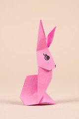 A pink origami rabbit on a beige background. Crafts for Easter, fold from paper, do it yourself.