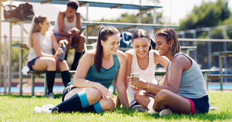 Sports, women and group outdoor, smartphone and connection with girls on field, chatting and relax. Fitness, female athletes smile and young ladies with cellphone, summer and on break after training