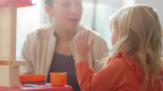 Mom and daughter performing role game about having diner, hot meal, family time. Ladies eating imaginary food, child got burn with hot food. Bright nursury with kitchen utensils and toy teaset. HQ 4k