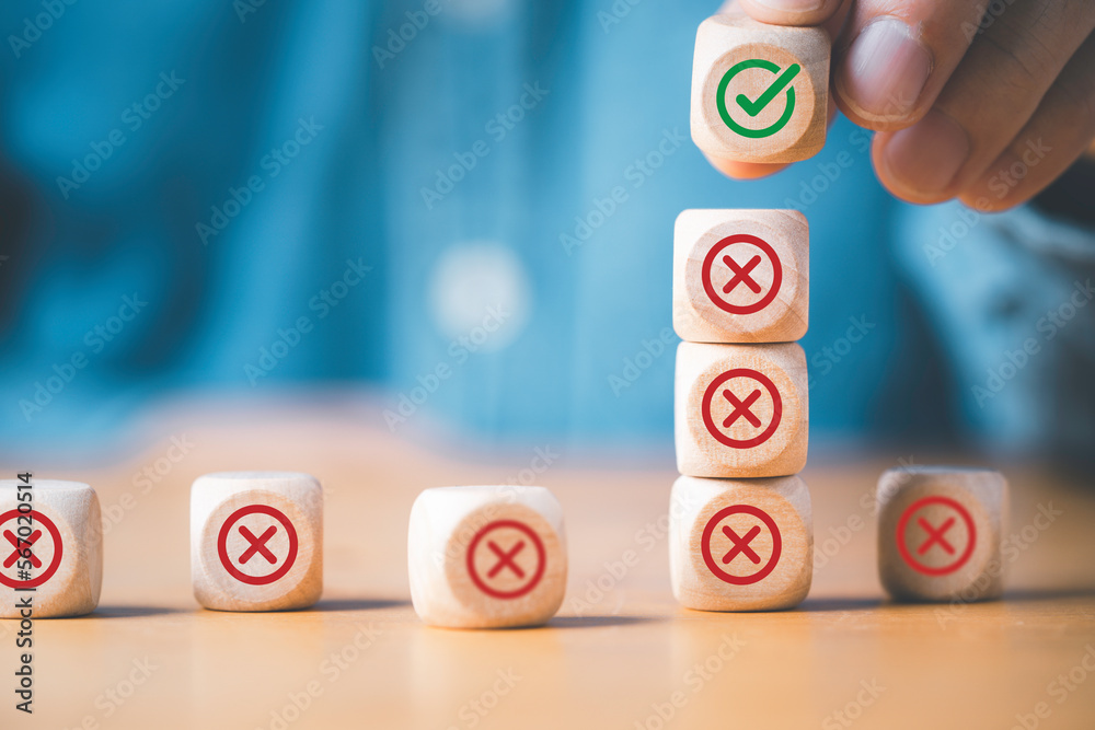 Poster Businessman stacking green correct sign mark on top of Red Cross mark which print screen on wooden cube block for approve and reject business proposal concept.