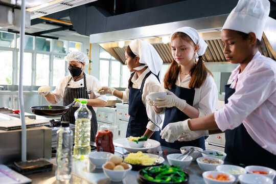 Senior asian woman chef teach student. Cooking class. culinary classroom. group of happy young woman multi-ethnic students are focusing on cooking lessons in a cooking school.