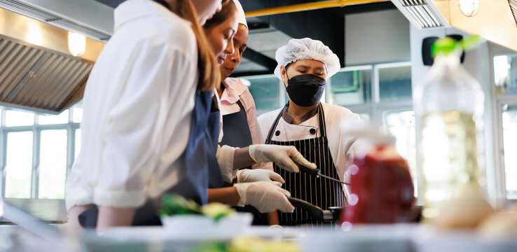 Senior asian woman chef teach student. Cooking class. culinary classroom. group of happy young woman multi-ethnic students are focusing on cooking lessons in a cooking school.