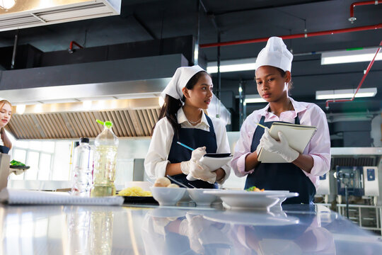 take note on book. Cooking class. culinary classroom. group of happy young woman multi-ethnic students are focusing on cooking lessons in a cooking school.