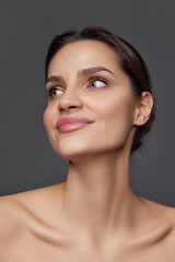 Fototapeta premium Anti-wrinkles care. Eco products. Beautiful brunette young girl with smooth well-kept skin posing over grey background. Concept of natural beauty, skin care, cosmetology, cosmetics, health, fashion