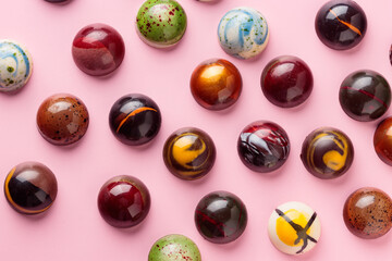 Assortment of painted handcrafted chocolate bonbons. Delicious dessert on a pastel pink solid...