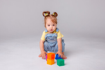 little baby girl is sitting on a white background and playing with colorful cubes. kid's play toy...