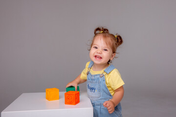 little baby girl is sitting on a white background and playing with colorful cubes. kid's play toy cubes
