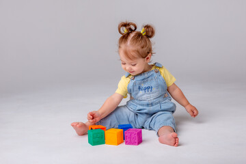 little baby girl is sitting on a white background and playing with colorful cubes. kid's play toy cubes
