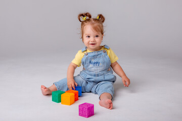 little baby girl is sitting on a white background and playing with colorful cubes. kid's play toy cubes
