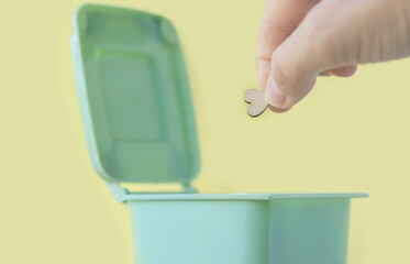 small mini wooden heart shape falling in mini small green color trash garbage bin can.against valentines day holiday no celebration february 14th disappointed upset.isolated on yellow background