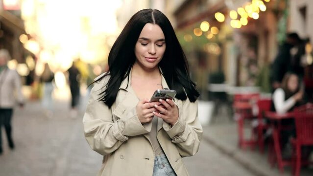 Gorgeous beautiful young woman with dark hair messaging on the smart-phone at the city street background