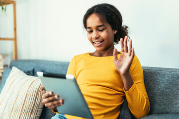 Happy African young girl using digital tablet technology sitting on couch at home.