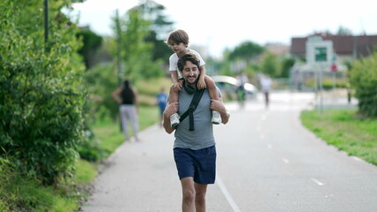 Son on father shoulders walking together outside. Child and parent bonding time walk in slow motion outdoors summer day