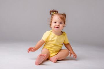 baby girl with yellow bodysuit sitting on a white background