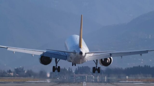 Back view airplane landing in airport, mountains in the background
