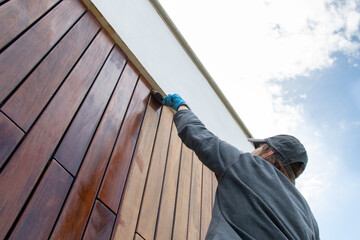 Staining the wood facade cladding with paint brush and protective oil, stain, house improvement...