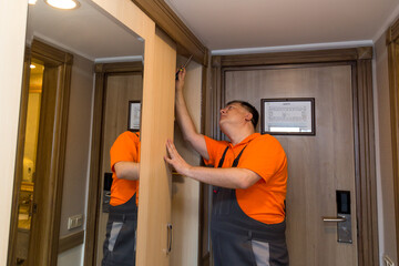 A male master in bright overalls installs a new wardrobe in the hotel.