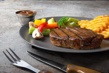 a piece of steak served with fried potato, vegetable, and brown sauce on a plate