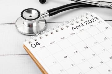 The April 2023 deskcalendar and medical stethoscope medical on wooden background, schedule to check up healthy concepts.