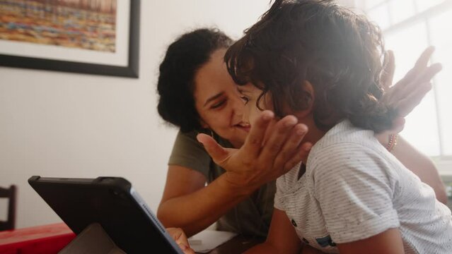 Caring mom using technology to homeschool her young son. This mother is helping her son learn from home by accessing e-learning resources using a digital tablet. Mother ensuring her child’s education