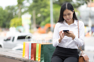 Female tourist in Thailand using a smartphone while waiting for a taxi after shopping in the city....