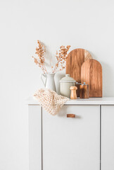 Cozy kitchen minimalism interior. Dishes, cutting boards, a jug of dried flowers on a white table